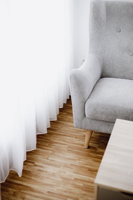 A close-up of a carpet cleaning vacuum cleaner head actively cleaning a patterned, cream-colored area rug in a room. The vacuum is black and modern, with a cable visible extending upward. The patterne